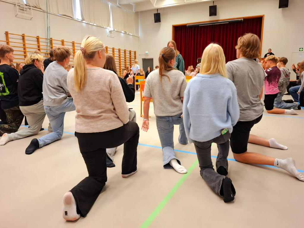 Paljon opiskelijoita polviseisonnassa liikuntasalissa.